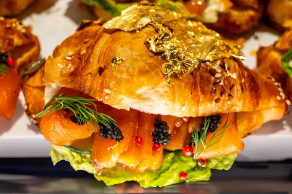 stock image Butter puff croissants on display in artisanal bakery in London, filled with Scottish smoked wild salmon fish and caviar, decorated with real 24 carat gold foil close up