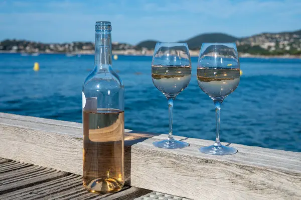stock image Glasses of cold rose wine from Provence served outdoor on wooden yacht pier with view on blue water and white sandy beach Plage de Pampelonne near Saint-Tropez, summer vacation in France