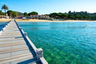 Morning view on crystal clear blue water and pier of Plage du Debarquement white sandy beach near Cavalaire-sur-Mer and La Croix-Valmer, summer vacation on French Riviera, Var, France clipart