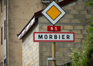 Morbier köyünde adı yazan yol tabelası, Fransız Morbier yarı yumuşak inek sütü peyniri üretimi, siyah küf tabakası, peynir turu ve Fransa 'da tatma.