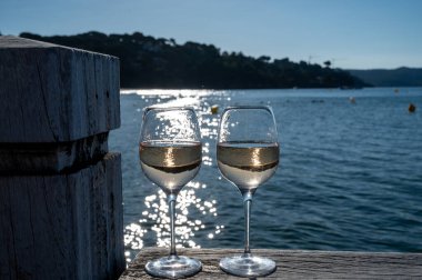 Glasses of cold rose wine from Provence served outdoor on wooden yacht pier with view on blue water and white sandy beach Plage de Pampelonne near Saint-Tropez, summer vacation in France