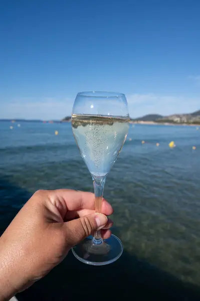 stock image Summer time in Provence, hand with glass of cold champagne cremant sparkling wine on famous Pampelonne white sandy beach near Saint-Tropez in sunny day, Var department, France, beach club party