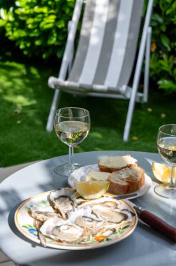 Fransa 'nın Gujan-Mestras limanındaki Arcachon körfezi istiridye çiftliği köyündeki restoranda taze çiğ istiridye kabukları, ekmek, tereyağı ve beyaz şarapla servis edilen tabaklar.