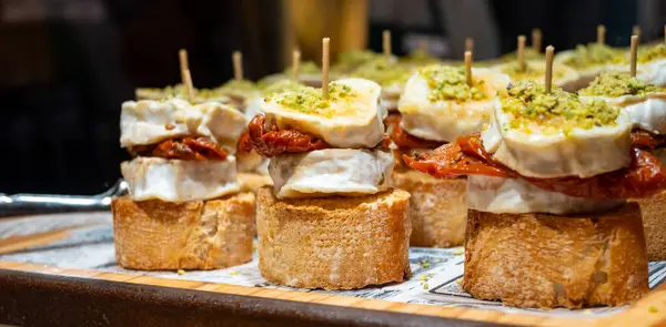 stock image Typical snacks of Basque Country, pinchos or pinxtos skewers with small pieces of bread, sundried tomatoes, goat cheese served in bar in San-Sebastian or Bilbao, Spain, close up