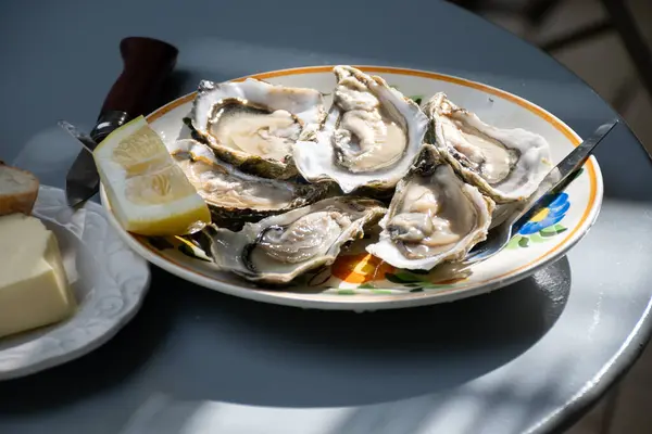 stock image Plate with fresh live raw oysters seashells with citron, bread, butter and white wine served at restaurant in oyster-farming village, Arcachon bay, Gujan-Mestras port, France