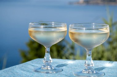 Cold sparkling wine, cava or champagne in two coupe glasses on table with blue sea view clipart