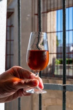 Hand with glass of sherry fino, manzanilla, wine, jerez fortified wine from palomino white grapes and andalusian window bars on background, Jerez de la Frontera, Spain clipart