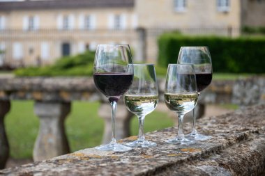 Glasses of white and red dry wine in old wine domain on Graves vineyards in Portets village and old castle on background, Bordeaux, France clipart