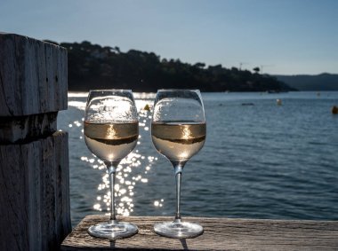 Glasses of cold rose wine from Provence served outdoor on wooden yacht pier with view on blue water and white sandy beach Plage de Pampelonne near Saint-Tropez, summer vacation in France