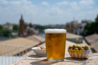 İspanyol birası bardakta ve çanakta yeşil Endülüs zeytinleri açık çatı terasında servis ediliyor. Eski Sevilla, Endülüs, İspanya 'nın merkezi manzaralı.
