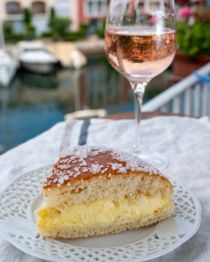 Fransız Riviera şarabı, bir bardak soğuk gül Cote de Provence şarabı ve Port Grimaud 'un yat limanında Tarte Tropezienne keki, Fransa' nın Provence şehrinde yaz tatili