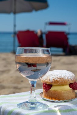 Lunch on sandy beach in Saint-Tropez with cake Tarte tropezienne filled brioche with cream and fresh red berries and glass of rose wine, summer vacation on sunny  French riviera, France clipart