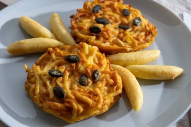 Pumpkin grated roasted patties, rosti or latkes and Fingernudel, finger potato noodle, dumplings decorated with pumpkin seeds close up clipart