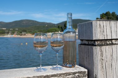 Bottle and glass of cold rose wine from Provence and wooden yacht boota pier on white sandy beach Plage de Pampelonne near Saint-Tropez, summer vacation in France, beach club party clipart