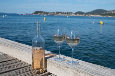 Glasses of cold rose wine from Provence served outdoor on wooden yacht pier with view on blue water and white sandy beach Plage de Pampelonne near Saint-Tropez, summer vacation in France