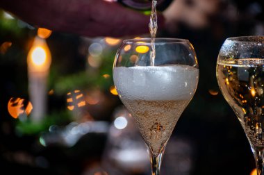 Yeni yıl ya da noel yemeği, bir bardak brut şampanya ya da kava, Prosecco köpüklü şarap ve arka planda Noel ağacı ve çelenk ışıkları, kutlama konsepti