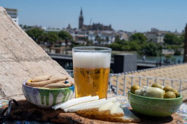 İspanyol birası, peyniri, tapas ve yeşil Endülüs zeytinleri yazın eski Sevilla, Endülüs, İspanya 'nın merkezi manzaralı terasında servis edilir.