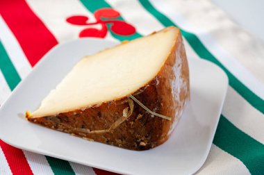 Piece of tasty Basque Brebis Fume smoked sheep cheese produced in south-western France, Northern Basque Country and towel with Basque symbol and colours close up clipart