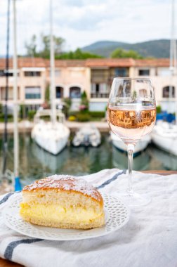 Fransız Riviera şarabı, bir bardak soğuk gül Cote de Provence şarabı ve Port Grimaud 'un yat limanında Tarte Tropezienne keki, Fransa' nın Provence şehrinde yaz tatili