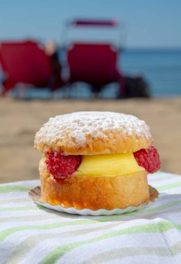 Lunch on sandy beach in Saint-Tropez with cake Tarte tropezienne filled brioche with cream and fresh red berries, summer vacation on sunny  French riviera, France clipart