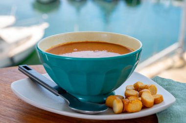 Homemade tasty fish or bisque soup with croutons served outdoor and view on yacht boats and houses of Port Grimaud, French Riviera, France. Food of Provence clipart