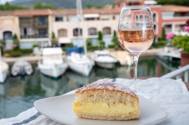 Fransız Riviera şarabı, bir bardak soğuk gül Cote de Provence şarabı ve Port Grimaud 'un yat limanında Tarte Tropezienne keki, Fransa' nın Provence şehrinde yaz tatili