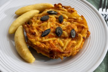 Pumpkin grated roasted patties, rosti or latkes and Fingernudel, finger potato noodle, dumplings decorated with pumpkin seeds close up clipart