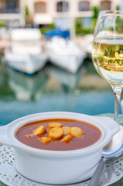 Homemade tasty fish or bisque soup with croutons served outdoor with glass of cold white wine and view on yacht boats and houses of Port Grimaud, French Riviera, France. Food of Provence clipart