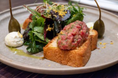 Alman restoranında terbiye edilmiş biftek tartartar çiğ eti, kızarmış ekmek ve tabakta yeşil salata ile servis edilir.
