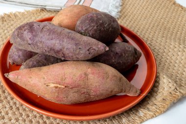 Renkli tatlı tadımlık tüberküloz kökleri mor ve turuncu organik tatlı patatesler, vejetaryen yemekleri, yakın plan.