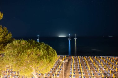 Sicilya 'da Palermo yakınlarındaki Mondello Sahili' ndeki güneşli yataklarda ve şemsiyelerde gece görüşü. Güzel, altın rengi kumlu, turkuaz suları ve büyüleyici villaları olan popüler sahil kenarı.