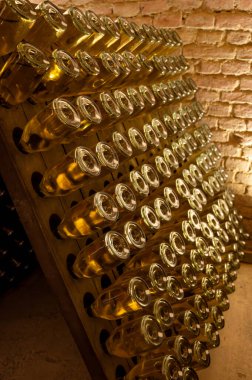 Derin ve uzun yeraltı mağaralarındaki raflarda şişeler şarap ve siyah üzümlerden şampanya yapıyor Reims, Champagne, Fransa 'da