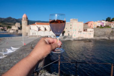 Güneş ışığında bir bardak gül Collioure AOC şarabı, Collioure kasabası manzaralı, renkli evler, kilise, kale ve plajlar, Occitanie, Fransa, turist beldesi