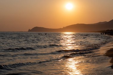 Güneş ışığında gün batımında yüzen insanların siluetleri, Sperlonga yakınlarındaki kumlu plajlar, Lazio, İtalya, yaz tatili
