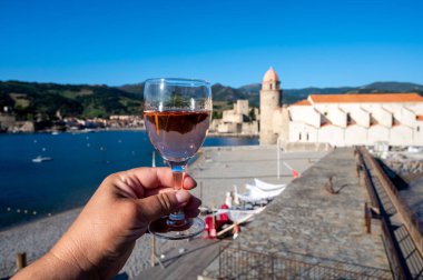 Güneş ışığında bir bardak gül Collioure AOC şarabı, Collioure kasabası manzaralı, renkli evler, kilise, kale ve plajlar, Occitanie, Fransa, turist beldesi