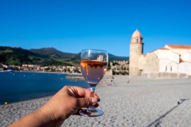 Güneş ışığında bir bardak gül Collioure AOC şarabı, Collioure kasabası manzaralı, renkli evler, kilise, kale ve plajlar, Occitanie, Fransa, turist beldesi