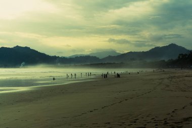 Kumsalda bulutlu bir öğleden sonra atmosferi var. Doğa deniz manzaralı, sinematik. Kızıl Ada Plajı (Pantai Pulau Merah), Banyuwangi, Doğu Java, Endonezya.