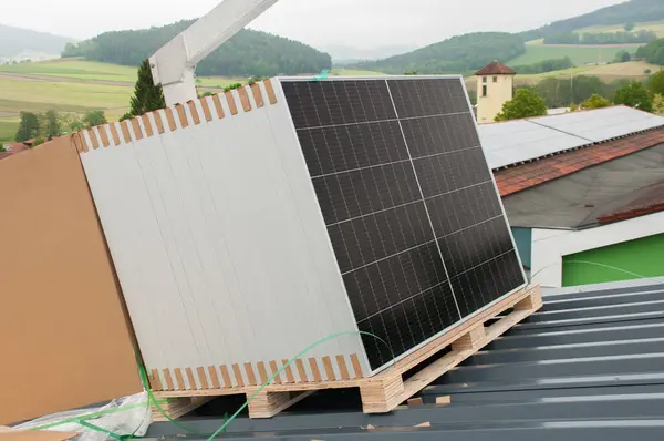 A crane lifts packaged solar panels onto the roof