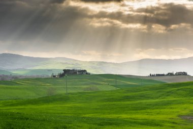 Amazing light beams among the clouds over the green fields of Tuscany countryside, Italy