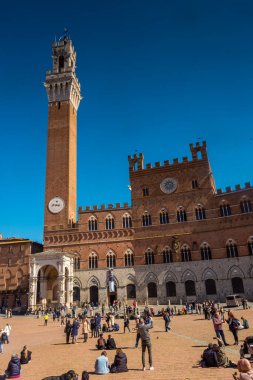 Siena, İtalya, 17 Nisan 2022: Turistler Piazza del Campo meydanının ve İtalya 'nın Siena kentindeki belediye binasının keyfini çıkarıyorlar. Siena 'nın tarihi merkezi UNESCO tarafından Dünya Mirası Alanı ilan edildi..