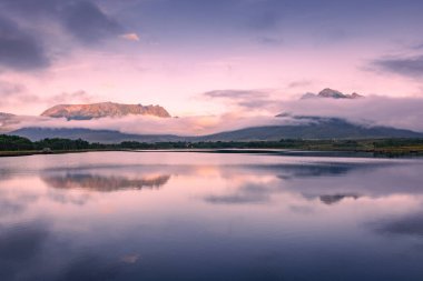 Spectacular reflection of the mountains on a lake with mist under the midnight sun, fairy tale atmosphere in the Vesteralen Islands, Norway
