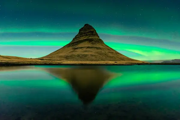 Spectacular reflection of the Kirkjufell mountain under the Northern Lights (Aurora Borealis) and starry sky in Iceland