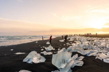 Jokulsarlon, İzlanda, 1 Aralık 2022: Elmas plajında gün batımına hayran olan turistler, buzdağlı volkanik plajlar