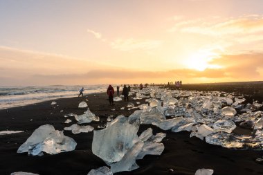 Jokulsarlon, İzlanda, 1 Aralık 2022: Elmas plajında gün batımına hayran olan turistler, buzdağlı volkanik plajlar