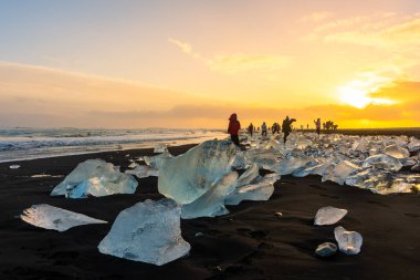 Jokulsarlon, İzlanda, 1 Aralık 2022: Elmas plajında gün batımına hayran olan turistler, buzdağlı volkanik plajlar