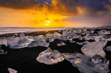 Elmas Sahili üzerinde inanılmaz bir gün batımı, İzlanda 'daki Jokulsarlon buzulundan gelen buzdağlarıyla volkanik kara plaj.