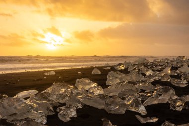 Elmas Sahili üzerinde inanılmaz bir gün batımı, İzlanda 'daki Jokulsarlon buzulundan gelen buzdağlarıyla volkanik kara plaj.