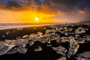 Elmas Sahili üzerinde inanılmaz bir gün batımı, İzlanda 'daki Jokulsarlon buzulundan gelen buzdağlarıyla volkanik kara plaj.