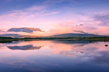 Spectacular reflection of the mountains on a lake with mist under the midnight sun, fairy tale atmosphere in the Vesteralen Islands, Norway