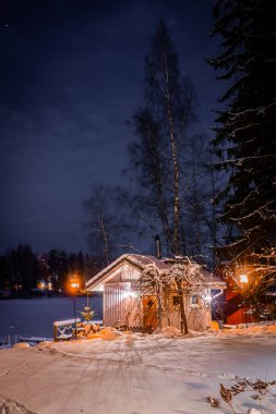 Donmuş bir gölün kıyısındaki yalnız ahşap kulübe. Finlandiya, Lempala 'da gece karlı manzaralar